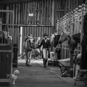 Man leading a horse walking through stables